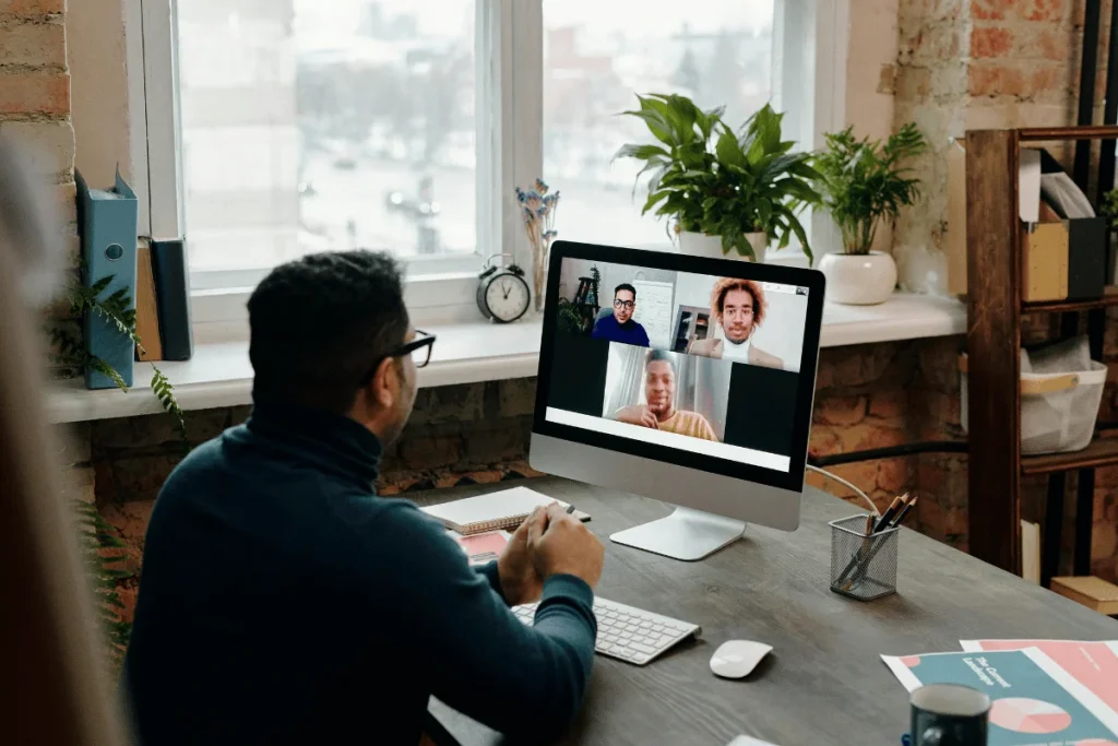 Man in glasses attending a virtual meeting with colleagues on a computer.