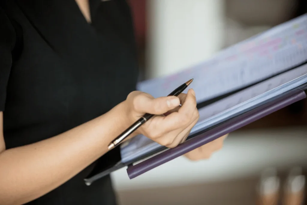 Person holding a pen and reviewing documents in a binder.