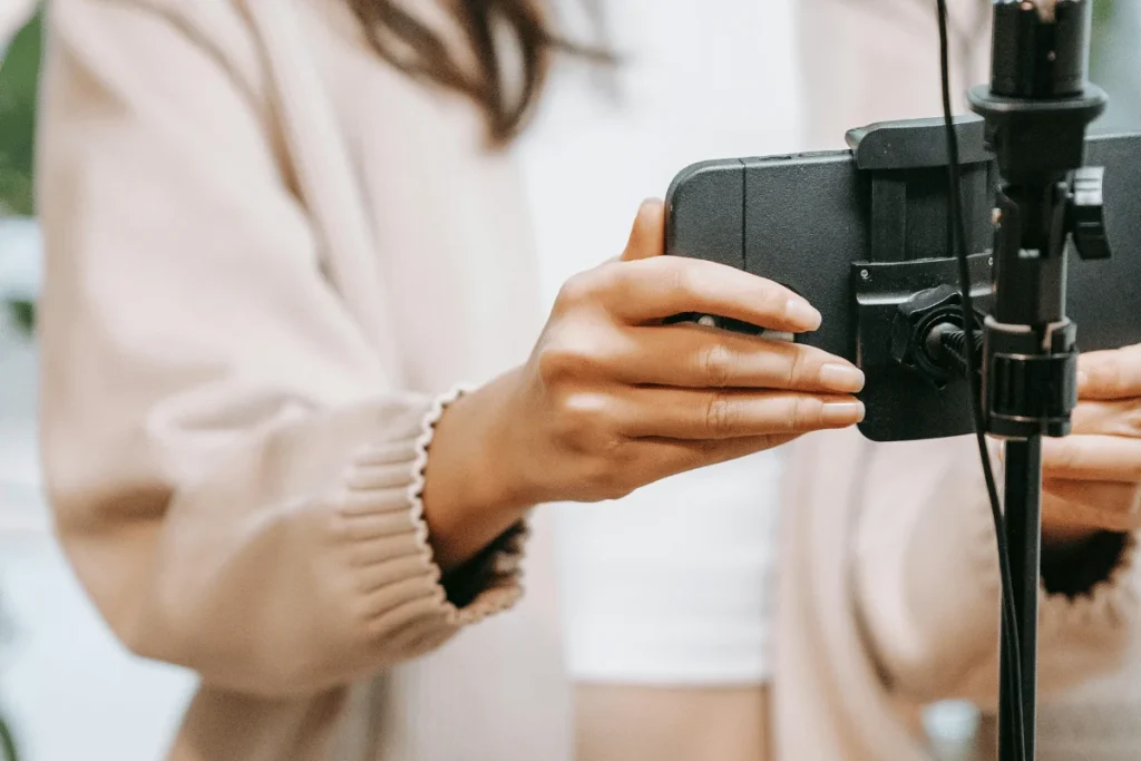 Close-up of a woman adjusting a smartphone on a tripod stand for recording video content.