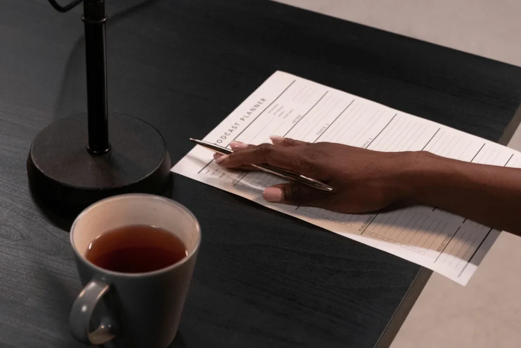 Close-up of handwritten notes on a podcast planner next to a half-full coffee cup.