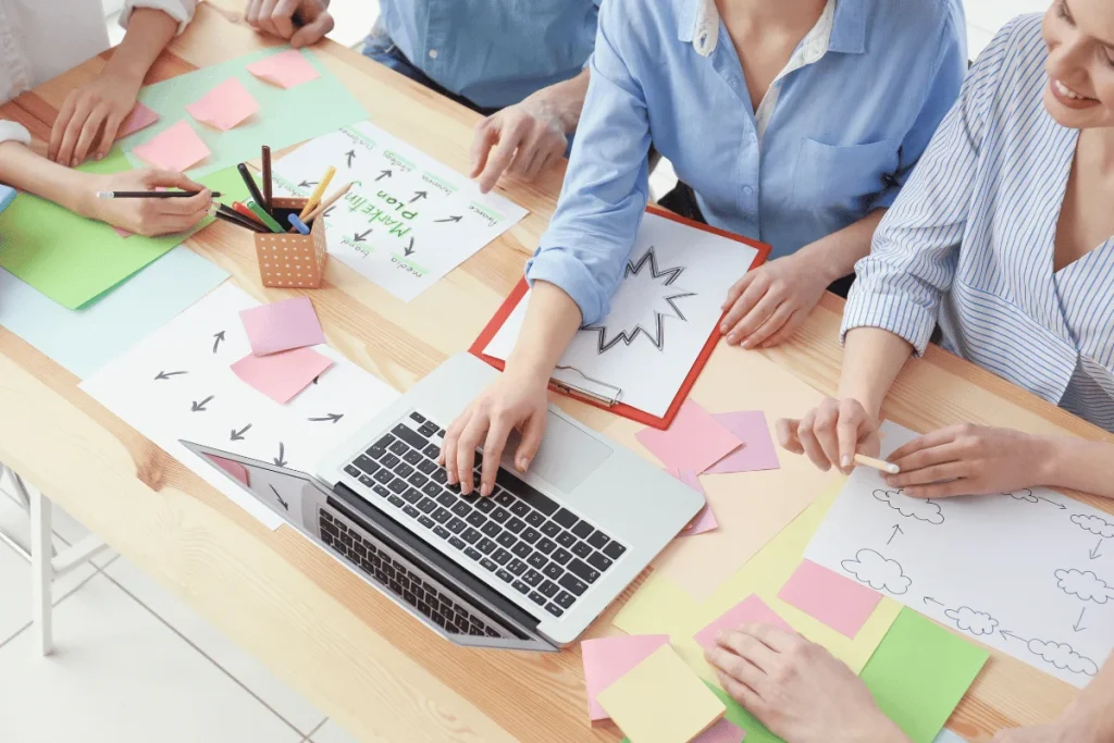 A group collaborating at a table with a laptop, papers, and sticky notes.