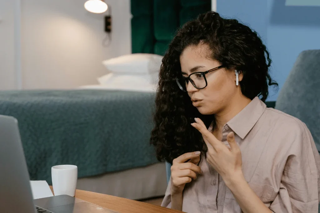 Person at a desk with a laptop and a white mug, wearing a wireless earpiece.