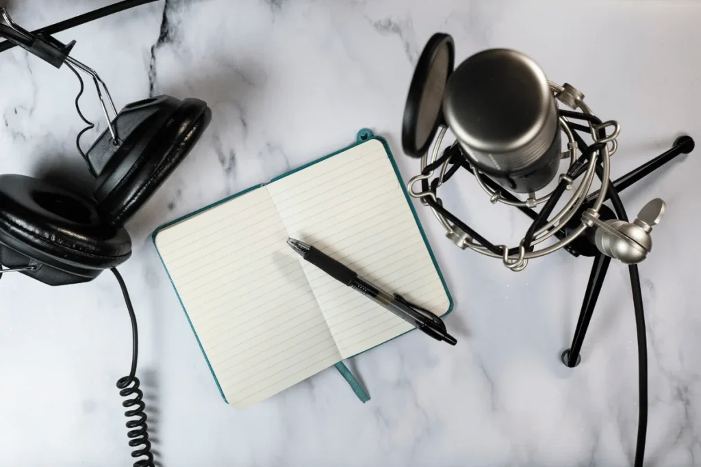 Headphones, a notebook with a pen, and a microphone on a marble surface.