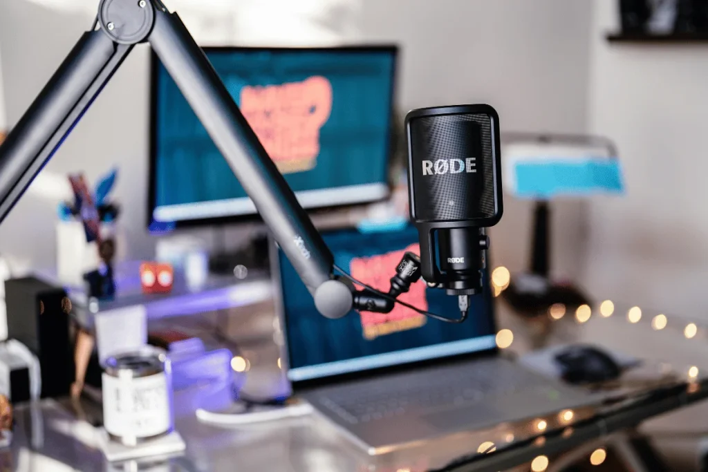 Focus on a RODE podcast mic with a blurry desktop and ambient lighting.