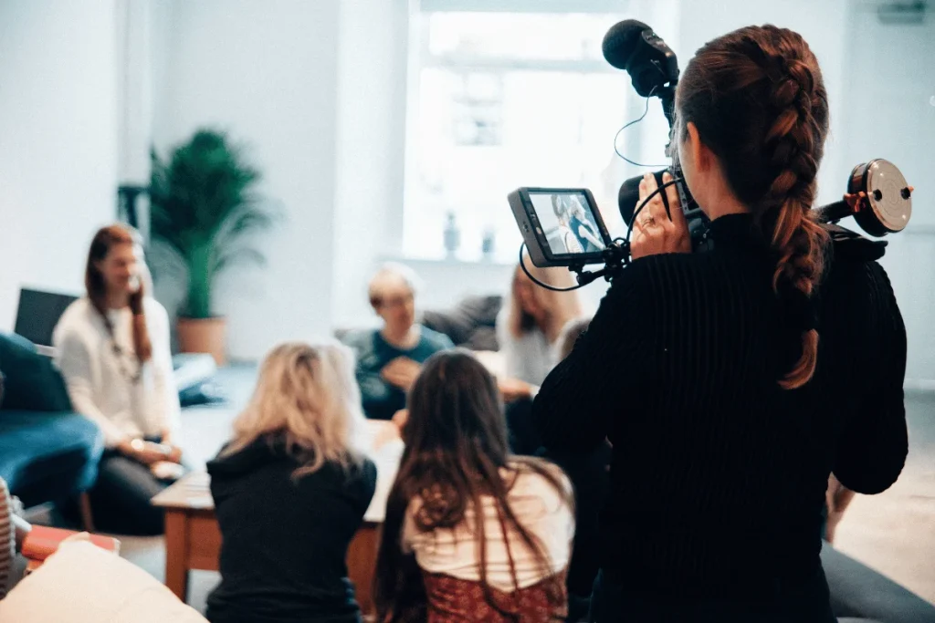 Filmmaker recording a group discussion using a professional video camera in a bright studio.