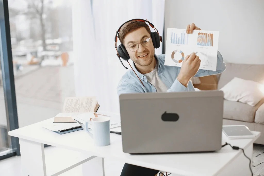 Man wearing headphones presenting charts during an online meeting at a home office.