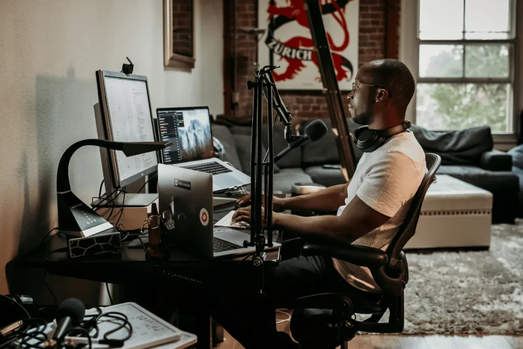 A person sits at a desk with multiple monitors and a microphone, engaged in work in a cozy, stylish workspace.