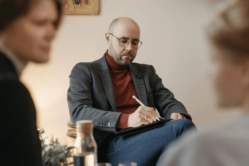 Man in glasses and a turtleneck taking notes during a business meeting, illustrating focused and professional work environment.