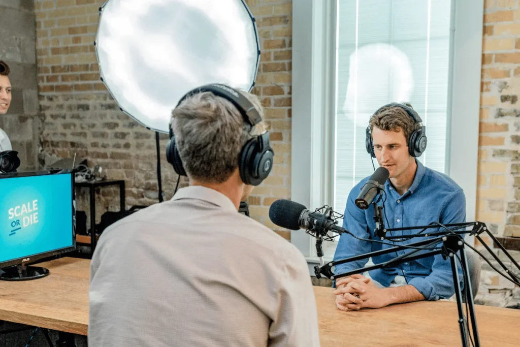 Recording a podcast episode with two men in headphones and microphones, professional studio environment.