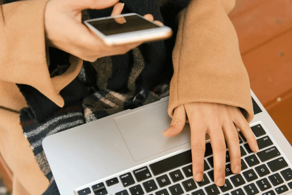 Overhead view of hands typing on a laptop while holding a smartphone.