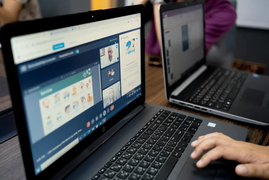 Two laptops on a desk displaying a video conference and data analytics.