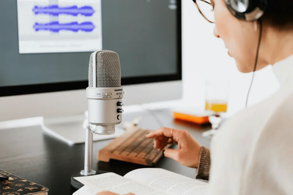 Podcaster recording audio with a professional microphone and computer setup.