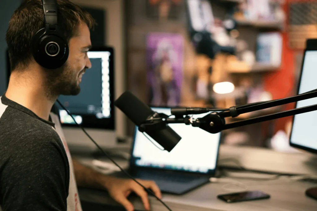 A person wearing headphones sits in front of multiple monitors, engaged in a recording session with a microphone nearby.