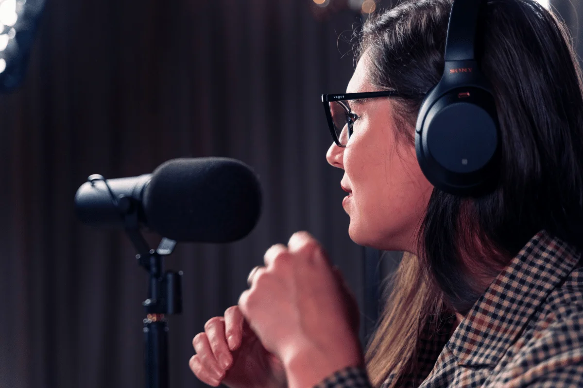 Female podcaster wearing headphones and speaking into a professional microphone.
