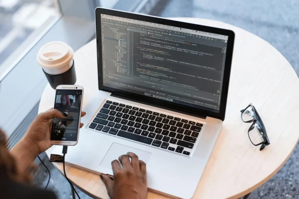 Hands typing on a laptop with code, holding a phone with a video.