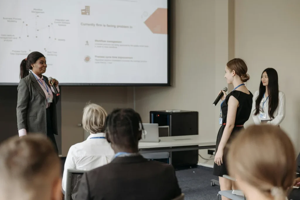 Businesswoman presenting a slideshow while engaging with an audience member holding a microphone.