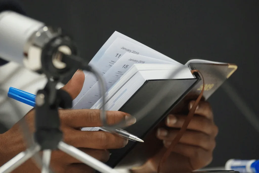 Close-up of hands holding a planner and pen during a podcast recording.