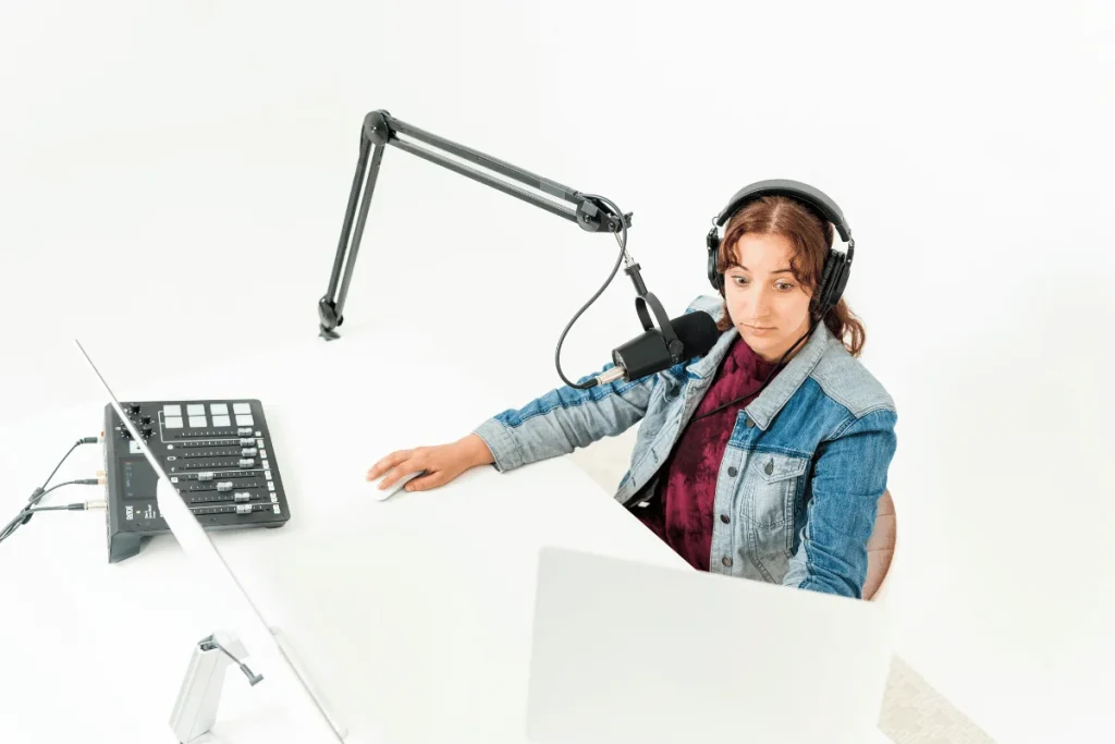 Female podcaster wearing headphones and speaking into a microphone in a minimalist studio.