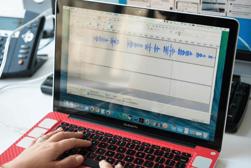 Person editing audio using Audacity software on a MacBook Pro.