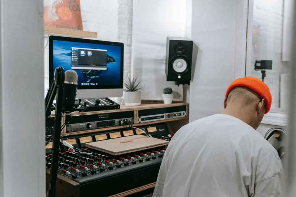 Audio engineer working at mixing console with iMac screen.