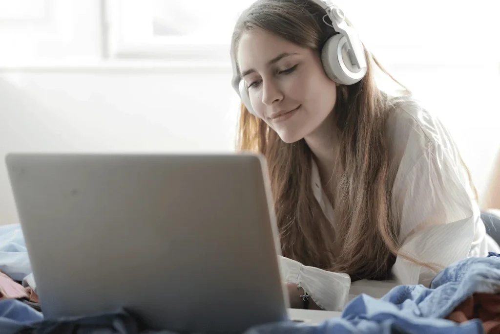 Smiling female with white headphones using a laptop, possibly engaged in remote work or study.