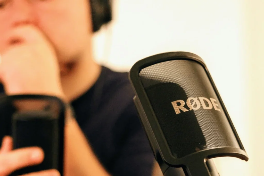 Close-up of RØDE microphone used for podcast recording with a person wearing headphones in the background.