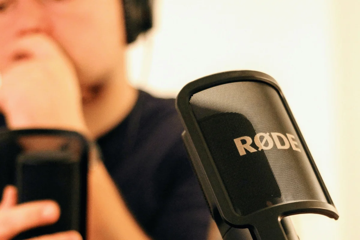 Close-up of RØDE microphone used for podcast recording with a person wearing headphones in the background.