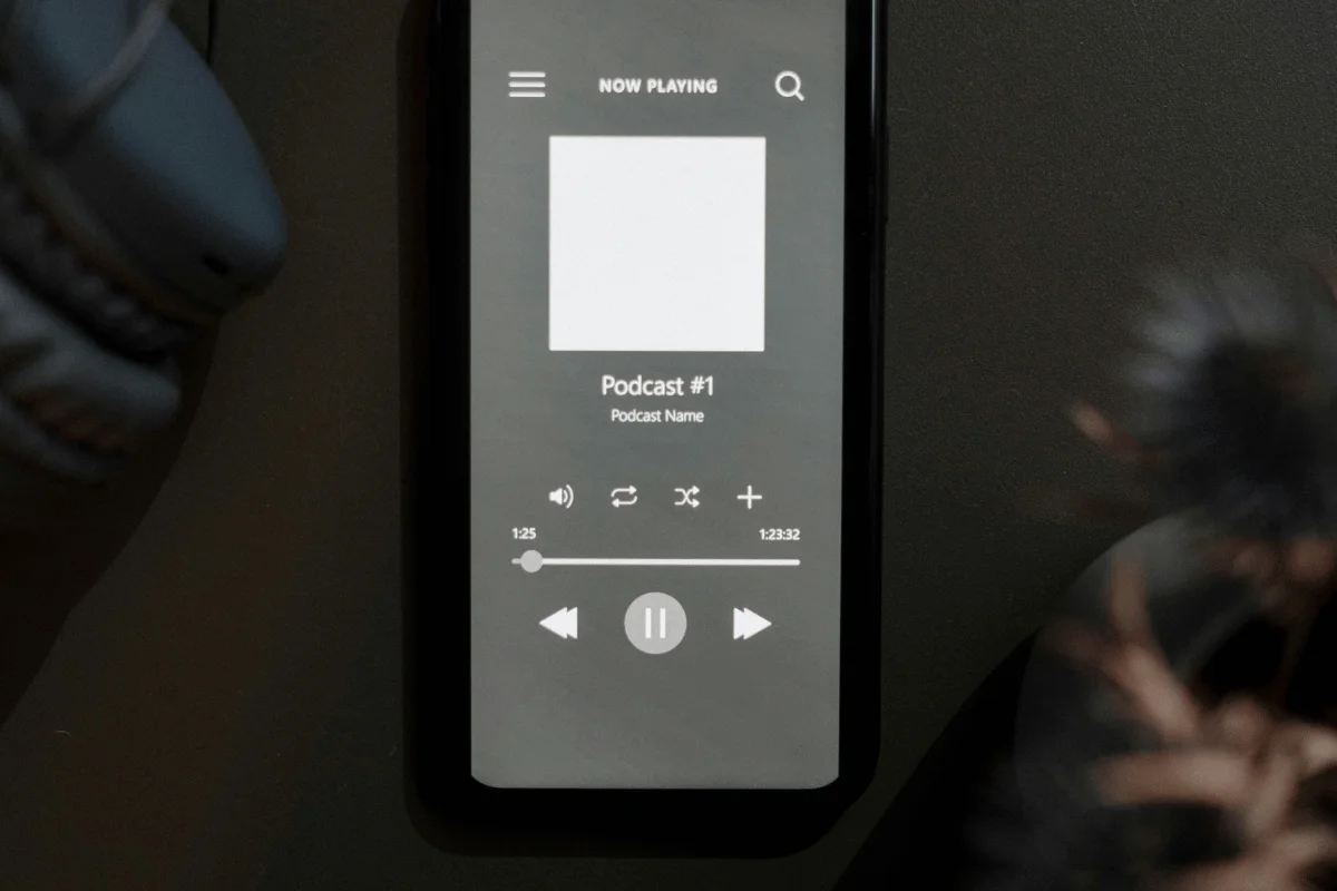 Close-up of a mobile phone screen with a podcast playing, earphones partially visible.