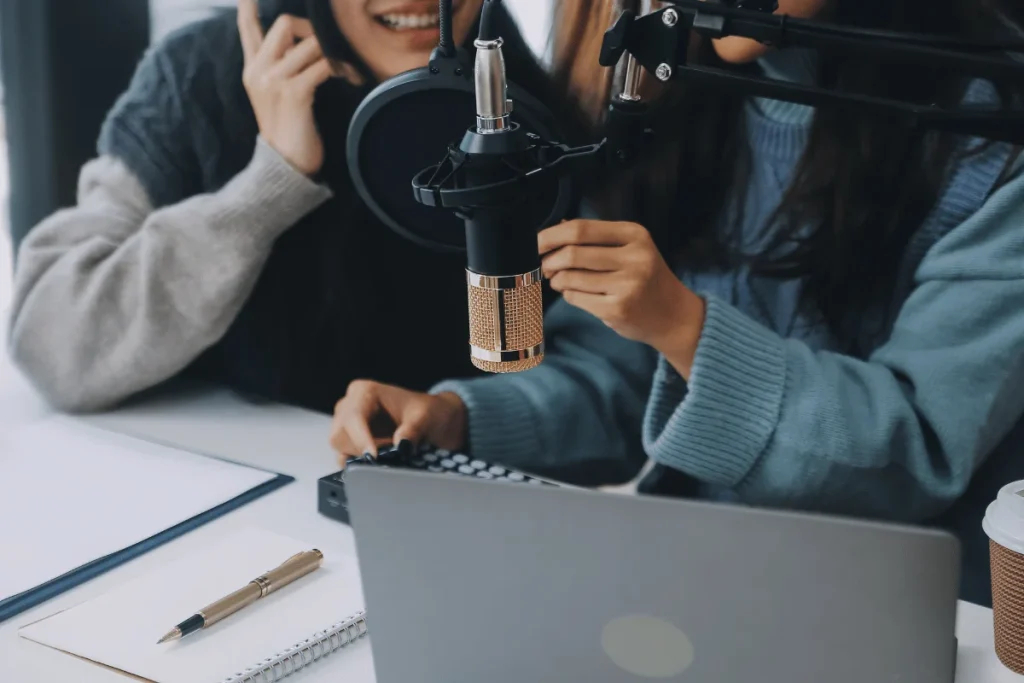 Female podcasters adjusting mic during recording session.