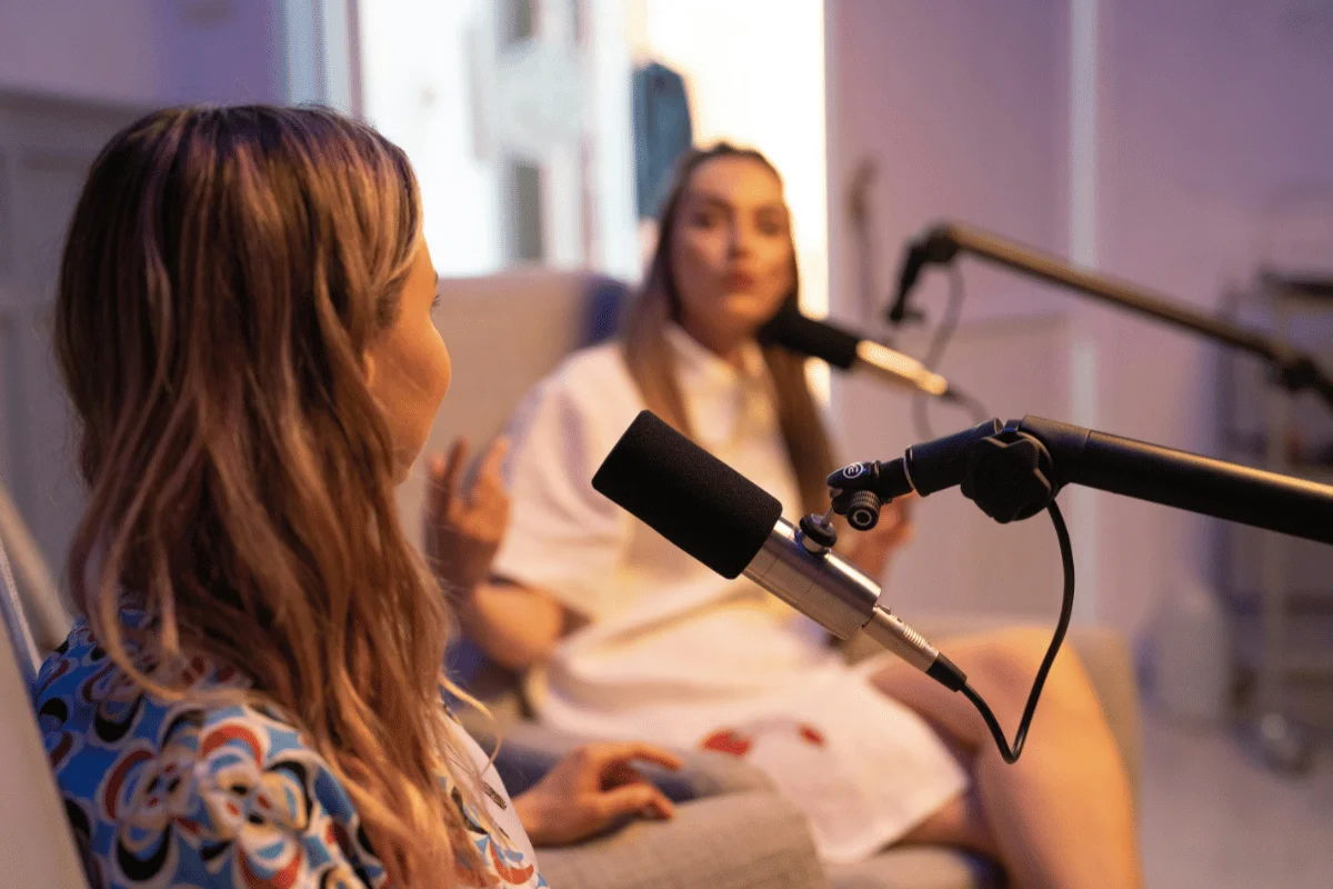 Close-up of two podcast microphones as women engage in a lively conversation in a creative environment.