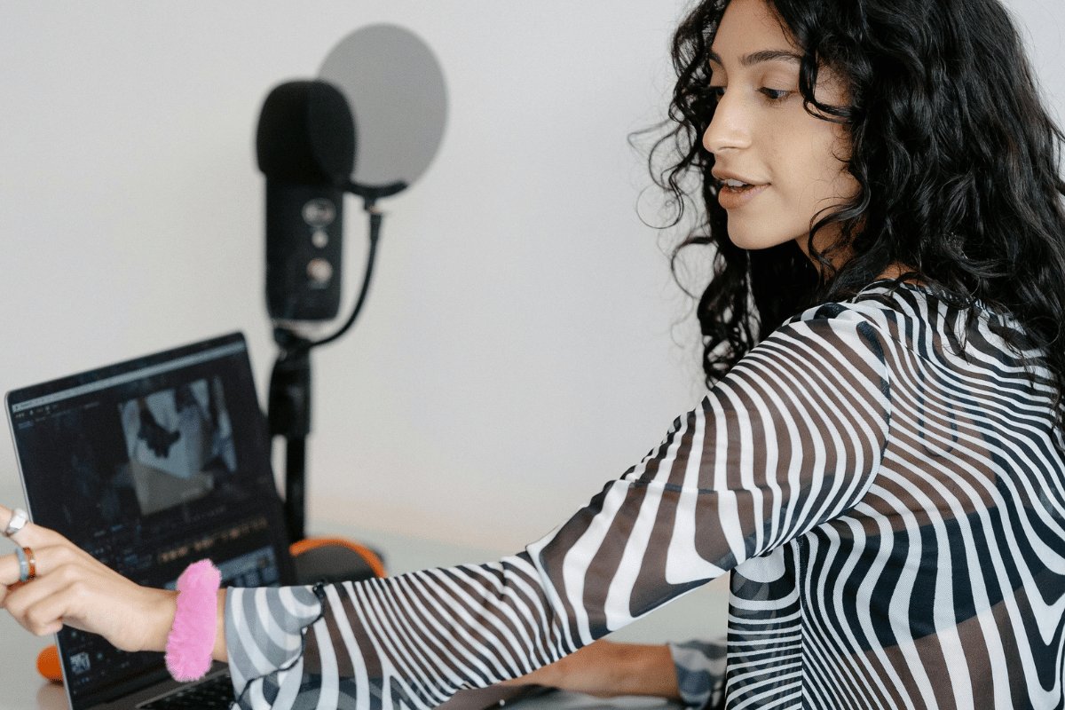 Woman editing video on laptop beside podcast microphone.