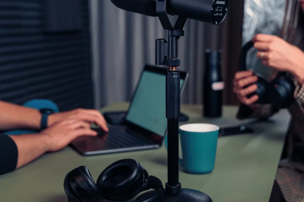 Close-up of a podcast recording setup with a microphone, laptop, and headphones.