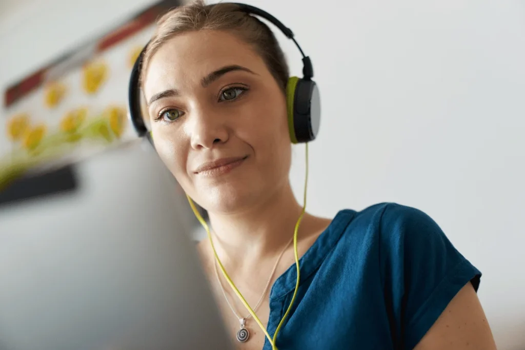 Woman with light green and black headphones looking at a laptop screen.
