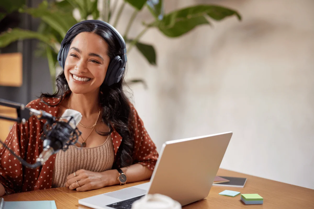 Female podcaster at a desk with a microphone, headphones, and laptop.