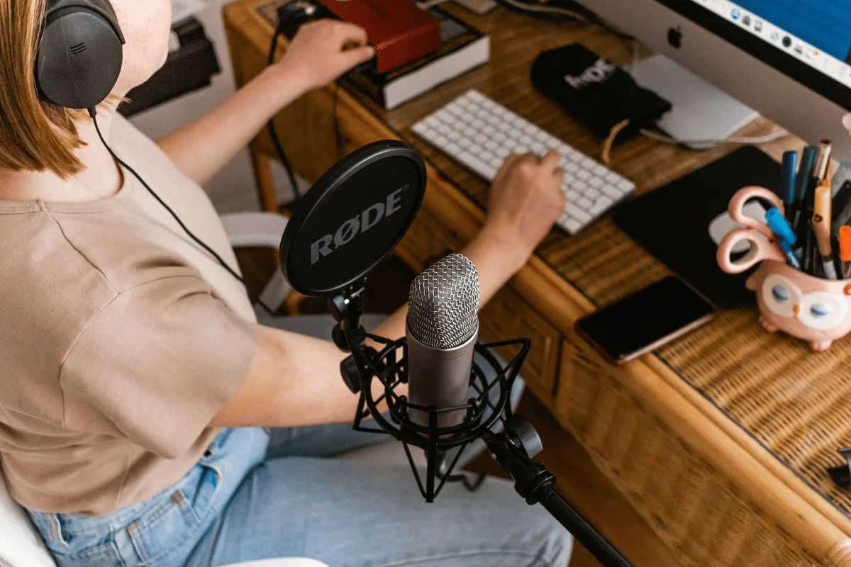Podcaster working on desktop computer with RØDE audio equipment.
