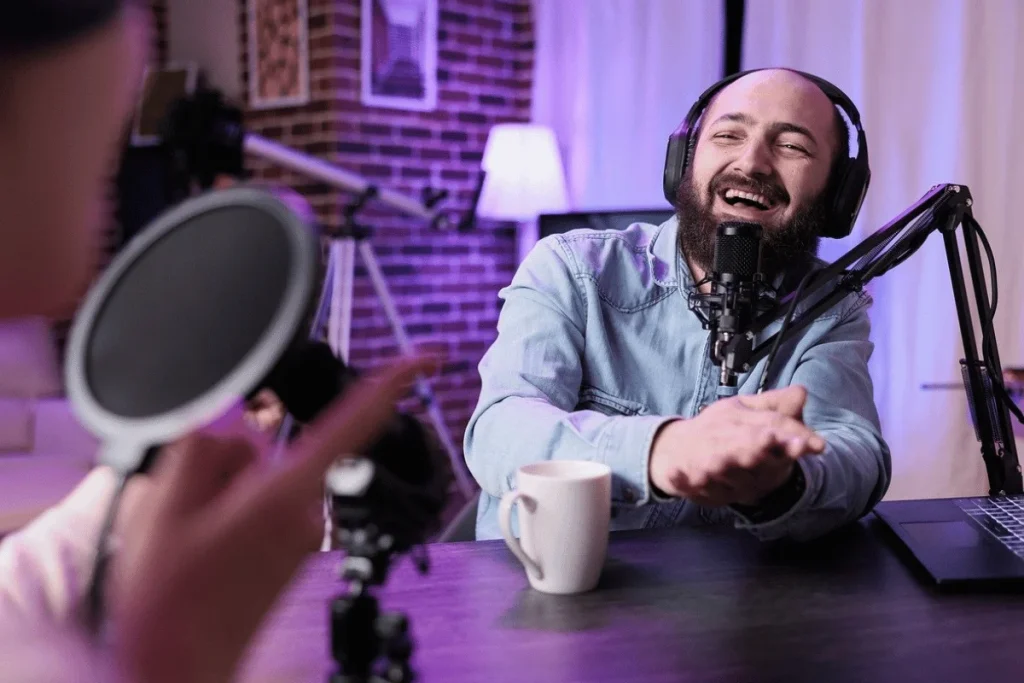 Podcast host laughing while recording with a professional microphone and headphones.
