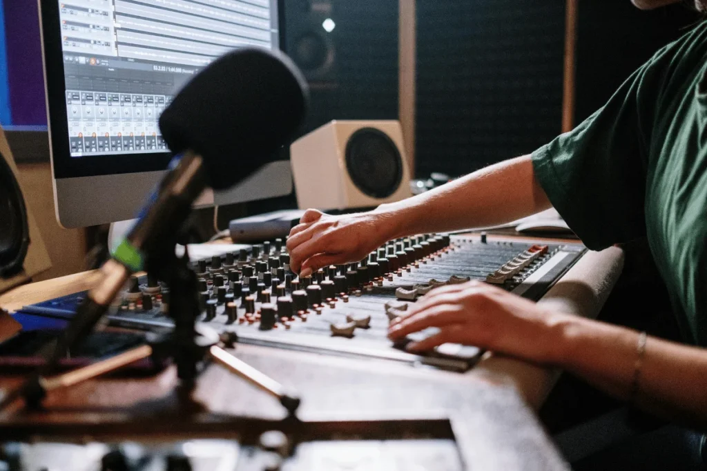 Male audio engineer adjusting controls on mixing console in professional recording studio.