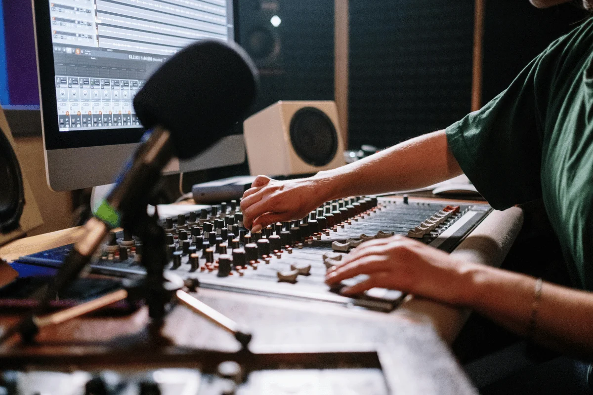 Male audio engineer adjusting controls on mixing console in professional recording studio.
