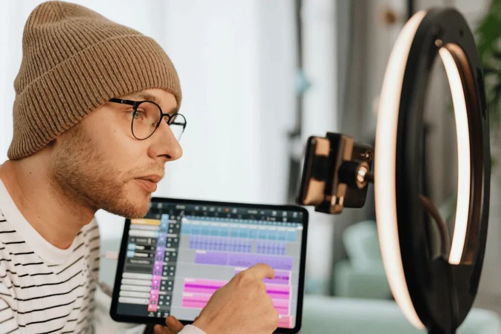 A person wearing glasses and a beanie is focused on a digital audio workstation on a tablet.