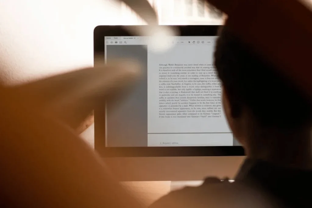 Person's hands holding tablet displaying text document with warm lighting and shadows in background.