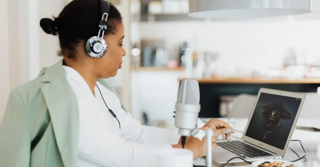 Woman with headphones working on laptop in kitchen creating Hello Audio personalized podcast feeds.