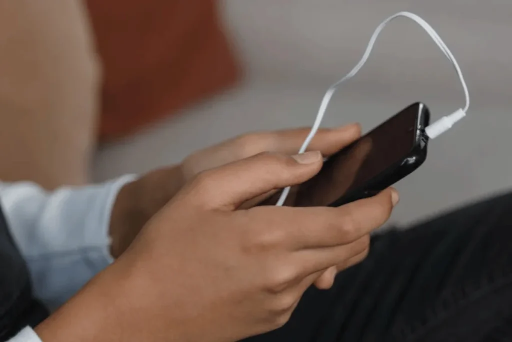 Hands holding smartphone with white earbuds connected, demonstrating Hello Audio convertkit integration setup.