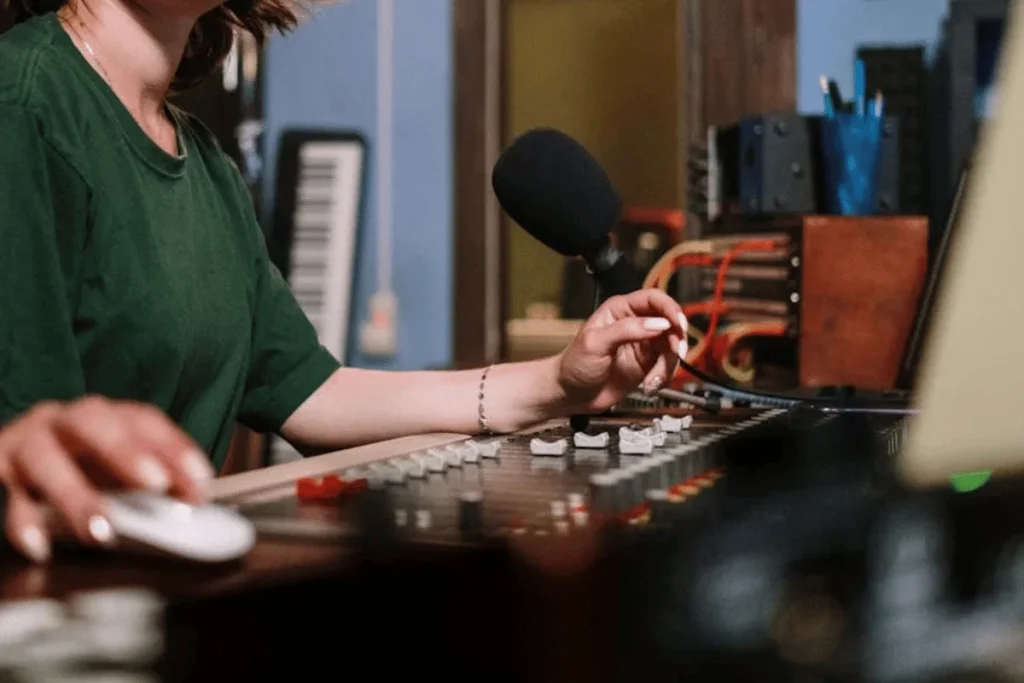 Woman in green shirt operating audio mixing console and laptop for hello audio convertkit integration setup.