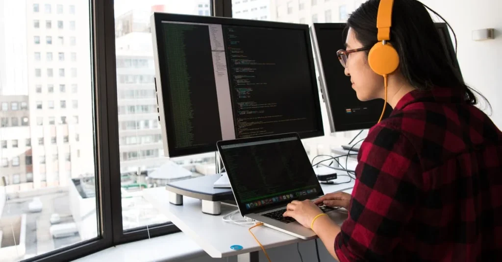 Developer coding with multiple monitors in modern office overlooking city buildings during thinkific vs podia comparison.