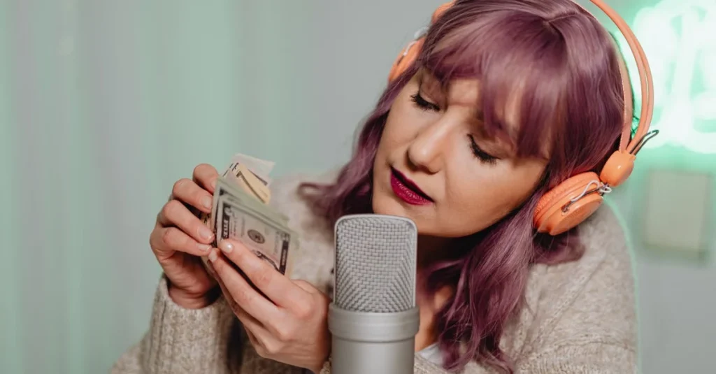 Woman with purple hair wearing orange headphones recording into studio microphone, holding cash notes.