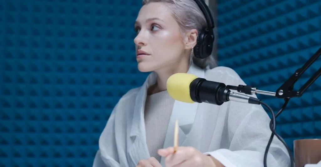 Woman speaking into yellow microphone with headphones in recording studio with blue acoustic foam wall.