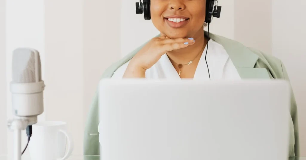 Smiling podcaster wearing headphones at laptop with microphone, exploring podcast hosting alternatives.