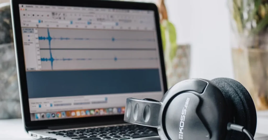 Professional headphones beside laptop running audio editing software with waveforms.