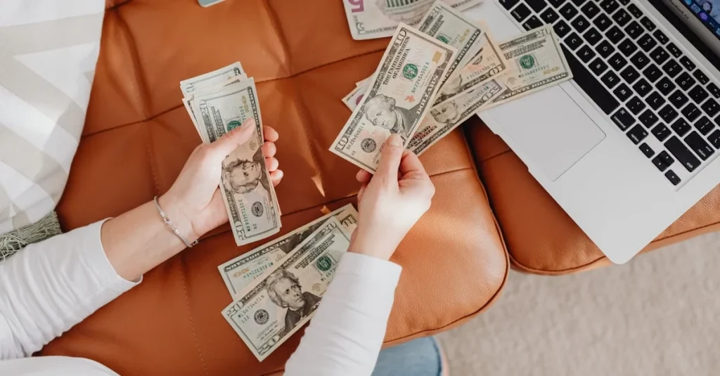Hands holding cash above laptop and brown bag, illustrating podcast hosting comparison revenue options.