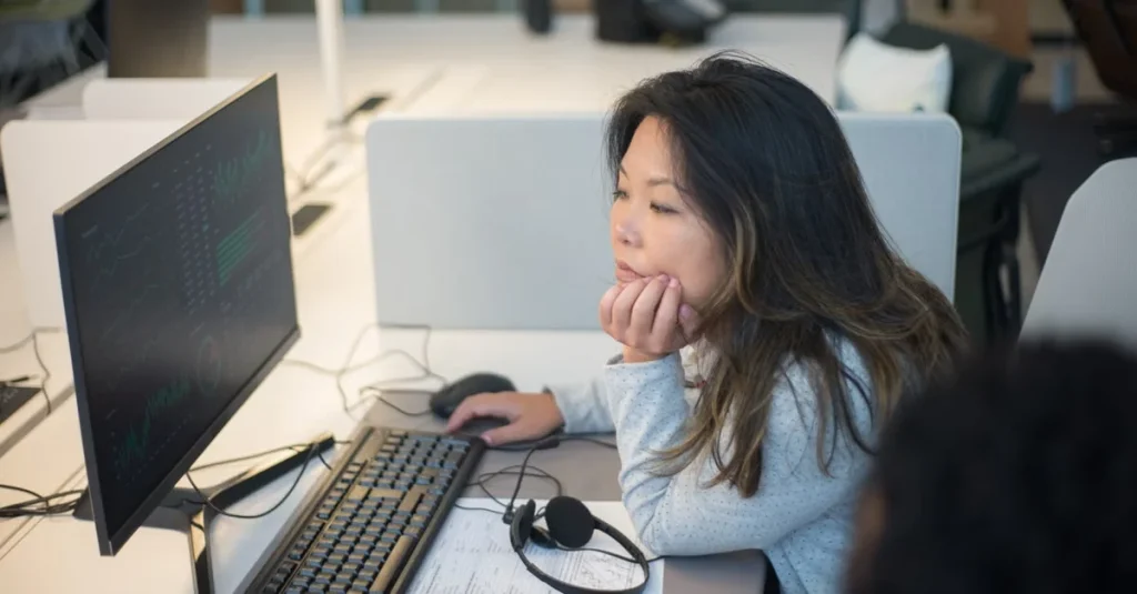 Woman using podcast software for mac on desktop computer at office workspace with monitor and keyboard.